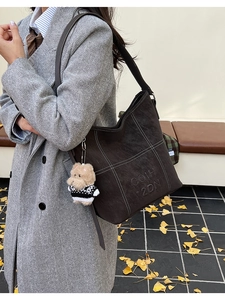 Dettaglio della borsa tote in pelle scamosciata marrone con cuciture bianche e orsetto