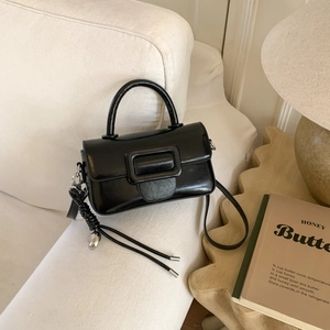 Detailed close-up of a vintage black leather crossbody bag with heart charm on a sofa