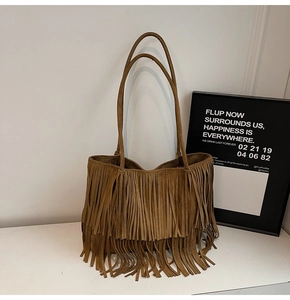 Detail of a brown suede tote bag featuring long bohemian tassels and smooth shoulder straps