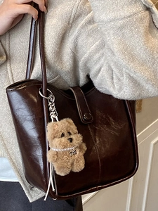 Minimalist dark brown glossy shoulder bag with a plush bear charm on a female model