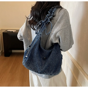 Detail of blue denim hobo bag featuring ruffled shoulder strap and side drawstring design