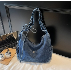 Detail view of denim shoulder bag featuring a metal M logo and ruched strap details
