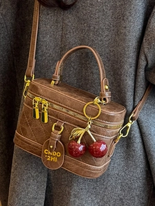 Vintage brown leather crossbody box bag with gold hardware and cherry charm on an overcoat