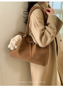Detail of vintage brown tote bag with belt buckle knot and plush ball on winter coat
