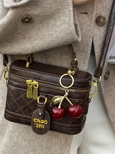 Dark brown quilted box bag with gold double zippers and a red cherry charm detail