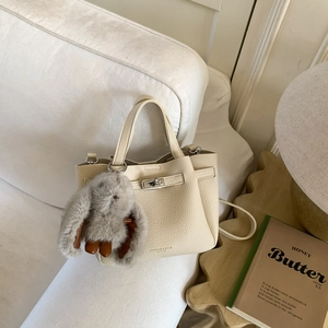 Vue détaillée du sac seau en cuir crème avec fermoir rotatif et breloque lapin en peluche