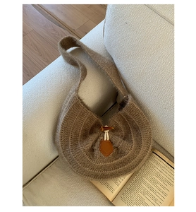 Close-up of a brown knitted hobo bag with a horn button detail on a white fabric sofa