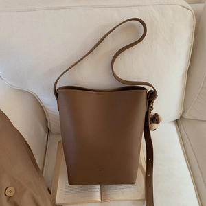 Detail of a brown lychee pattern leather bucket bag with a cute plush bear charm