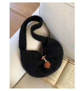 Detail of black faux fur crescent bag featuring a wooden toggle button closure on sofa