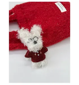 Close-up of a white plush dog pendant with glasses and a red sweater on a tote bag