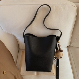 Detail of black pebbled leather bucket bag with cute plush bear charm on white sofa