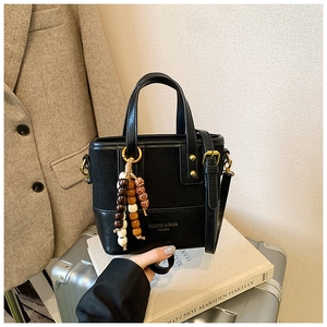 Close-up of black mixed-leather crossbody bag with vintage wooden bead tassel and logo detail