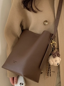 Brown leather bucket bag with dog pendant shown on a shoulder in a stylish autumn outfit