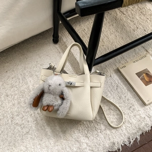 Détail du sac seau en cuir blanc cassé avec fermoir rotatif argenté et breloque lapin en peluche
