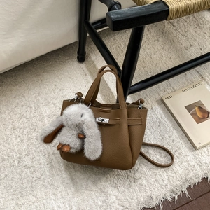 Détail du sac seau en cuir grainé marron avec un pendentif lapin blanc en peluche doux