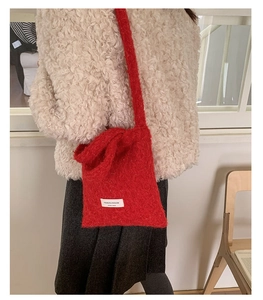 Detail of a red plush knit crossbody bag featuring a white designer brand label on front