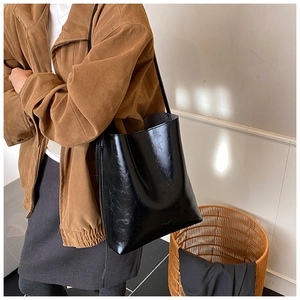 Detail view of large black glossy leather tote bag with thin straps and subtle logo