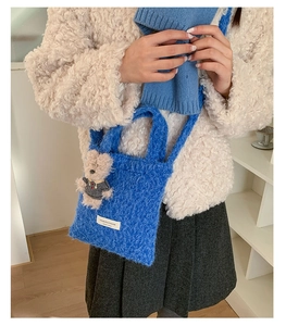 Detailed shot of a blue plush tote bag featuring a cute teddy bear charm and brand label