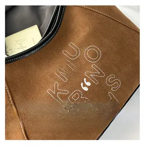 Macro view of brown suede tote with white contrast stitching and embroidered letters