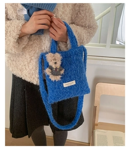 Detailed view of blue plush tote bag with cute bear charm and woven label on model