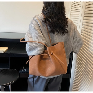 Detail of caramel brown leather tote bag with knotted shoulder strap worn by a model