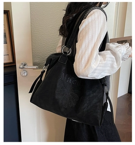Detailed view of daisy floral embroidery and metallic ring buckles on a black tote bag