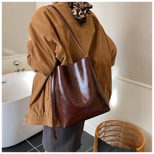 Close-up of a large dark brown leather bucket bag worn as a shoulder bag on a model