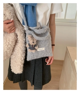 Close-up of gray plush shoulder bag featuring a cute teddy bear pendant and logo label