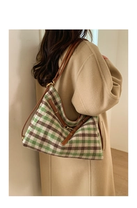 Detail of green plaid tote bag showing brown leather strap and golden metal buckle
