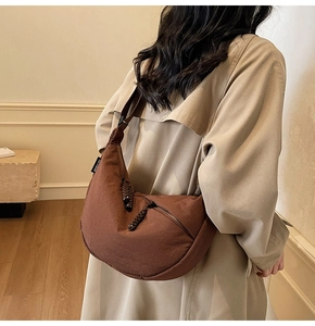 Detail view of brown canvas half-moon bag with woven zipper pull worn by model