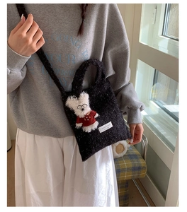 Detail of black tweed texture bag featuring a plush white bunny charm and logo tag