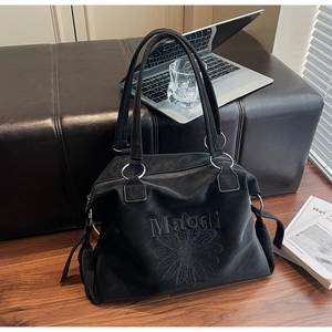 Detail view of a black tote bag featuring daisy embroidery and metallic ring accents