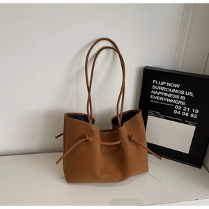 Detail of caramel leather tote bag showing side drawstring knots and matte texture