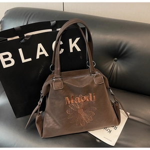 Detail of dark brown tote bag showing floral embroidery, Maodi logo, and silver rings