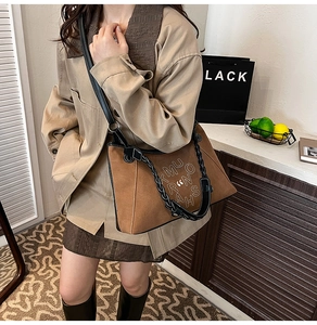 Detail of a brown suede crossbody bag with white embroidery and thick woven handle