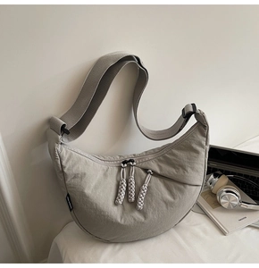 Detail of grey crescent bag showing woven rope zipper pull and adjustable wide shoulder strap