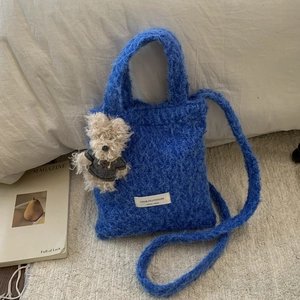Close-up of fluffy blue plush shoulder bag with cute puppy pendant on white background