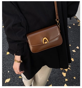Close-up of brown leather bag with gold U-shaped buckle against autumn leaves