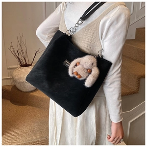 Detail of black suede tote bag with metal chain strap and cute plush rabbit charm