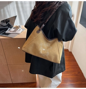 Detail of yellow suede tote bag with woven strap and white embroidered lettering on a model