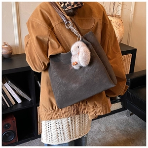 Detail view of charcoal grey suede tote bag featuring a plush bunny charm and chain strap