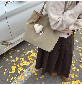 Close-up of khaki green leather tote bag with heart charm on a fall background