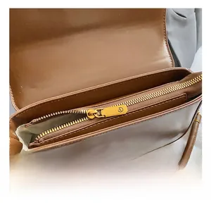 Detail view of the brown leather shoulder bag featuring gold metal zipper and logo puller