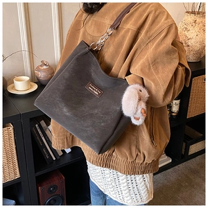 Detail of dark brown suede tote bag with metal chain strap and beige bunny charm