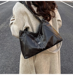 Close-up of black tote bag featuring contrast white stitching and woven leather strap