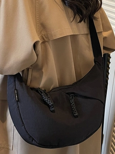 Minimalist black half-moon canvas crossbody bag worn by a model over a stylish beige coat