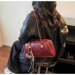 Bolso de hombro burdeos con colgante de bola dorada mostrado por una modelo en interior