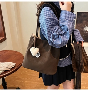 Detail of a large brown suede shoulder bag with a white heart plush charm on the side