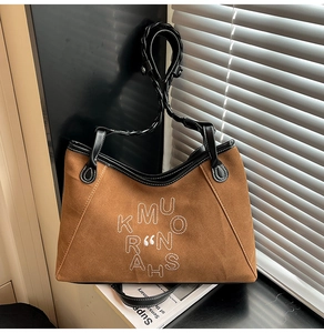 Detail of dark brown suede tote bag featuring white contrast stitching and woven black handles
