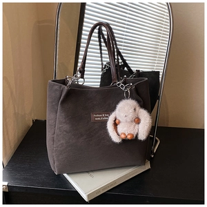 Detail of a large brown tote bag featuring a plush rabbit charm on a hardcover book